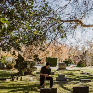 A person sits quietly in a cemetery, deep in reflection and mourning for a lost loved one.