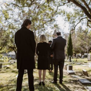 Mourners stand among gravestones in a tranquil cemetery, paying respects.