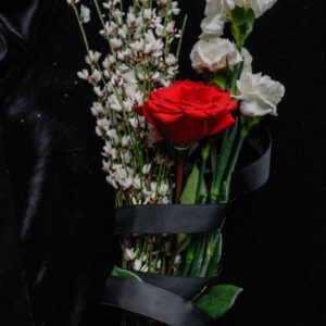 A moody bouquet featuring red and white flowers symbolizing loss on a black fabric background.