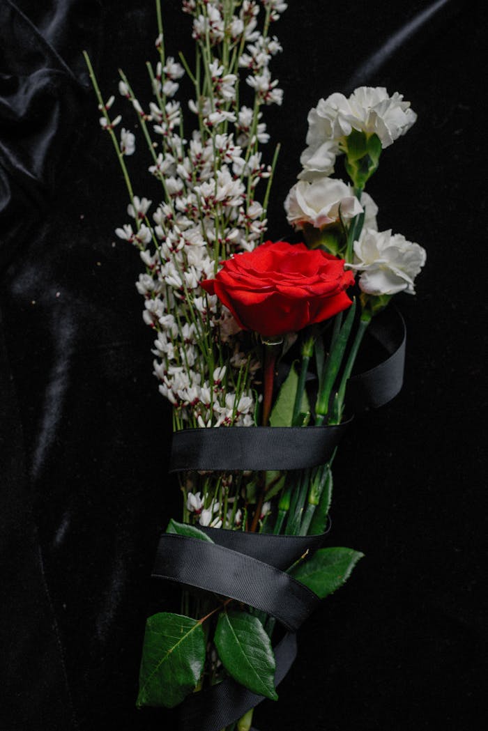 A moody bouquet featuring red and white flowers symbolizing loss on a black fabric background.